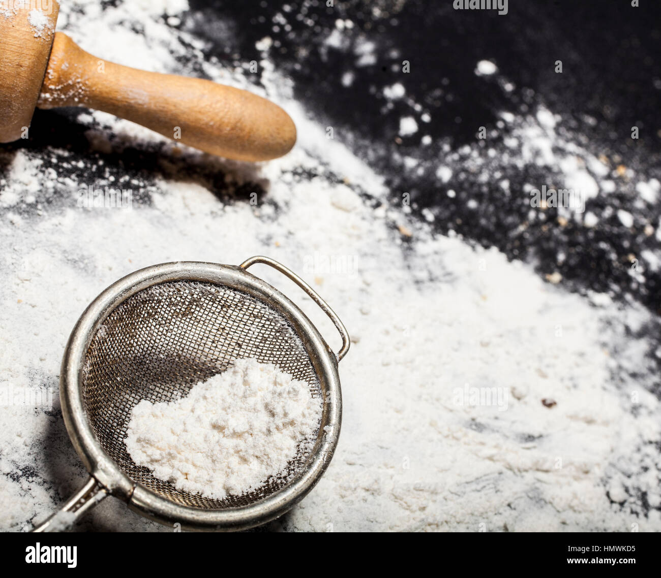 Metall Sieb und Nudelholz mit Mehl auf einem schwarzen Hintergrund zu verschütten. Stockfoto