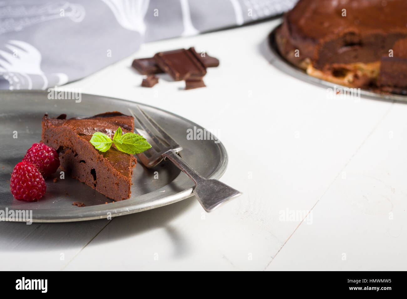 Schokoladenkuchen mit Himbeeren und Blatt Minze, ist Stück lag auf Teller mit Gabel, im Hintergrund runden Kuchen. Stockfoto