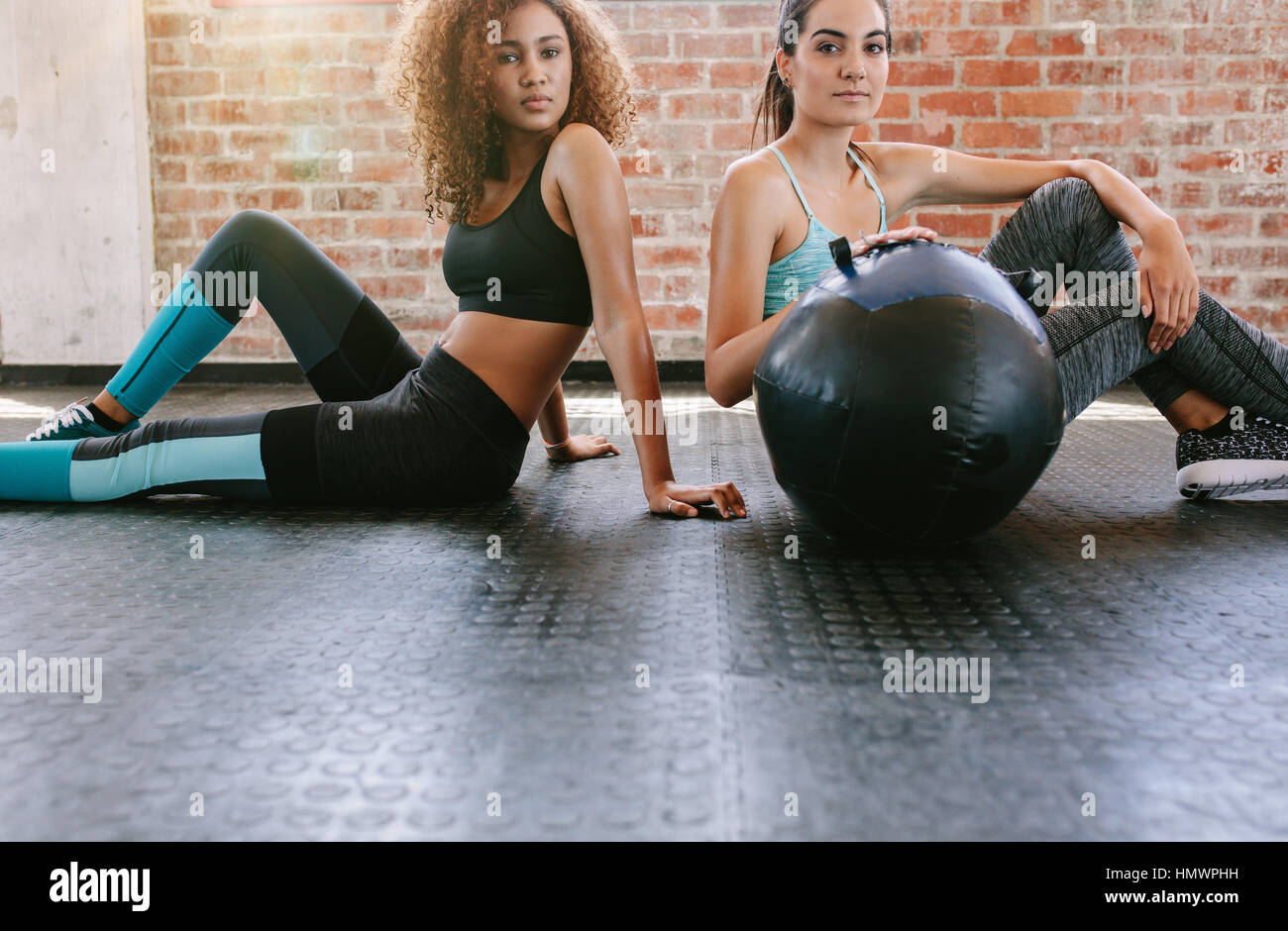 Porträt von zwei jungen Frauen sitzen im Fitness-Studio-Stock mit Medizinball. Gemischte Rassen Hündinnen im Fitnessraum. Stockfoto