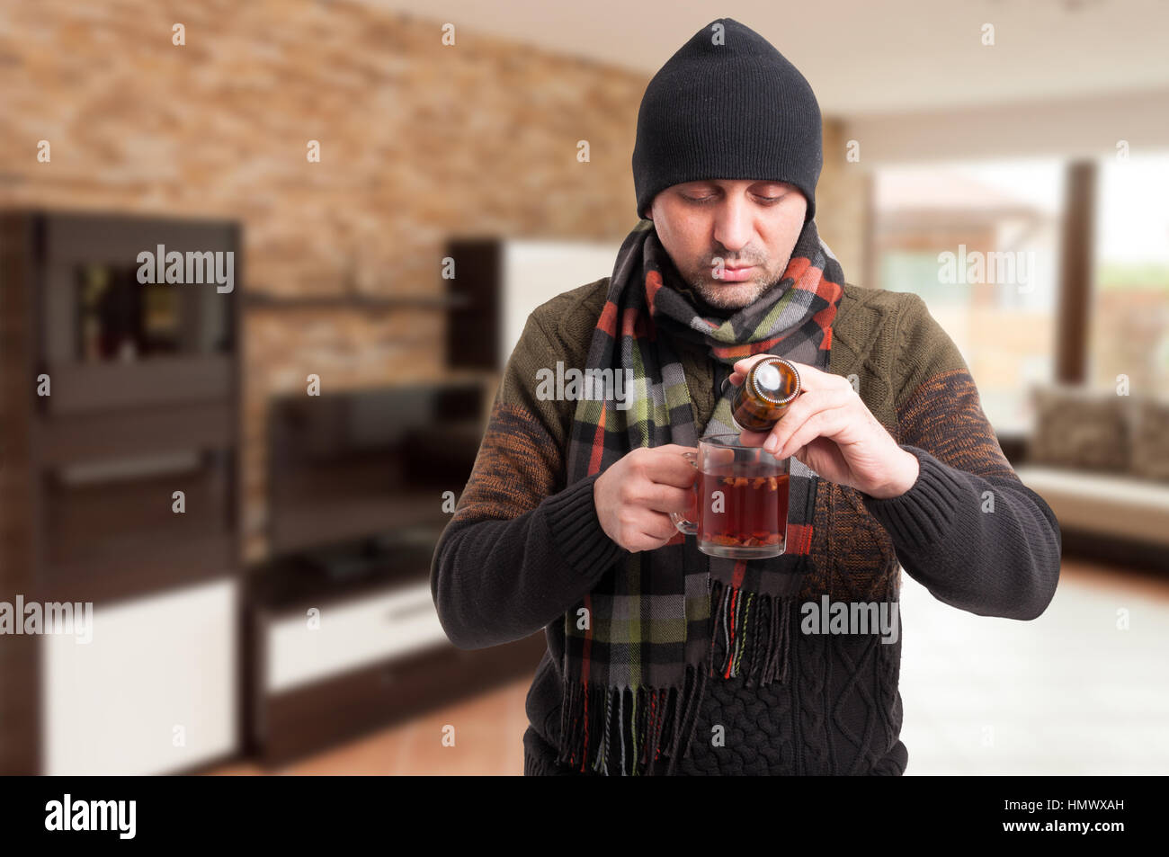 Kranker Mann Medikamente in seinem Tee im Inneren des Hauses als Grippe Behandlungskonzept mit textfreiraum Text setzen Stockfoto