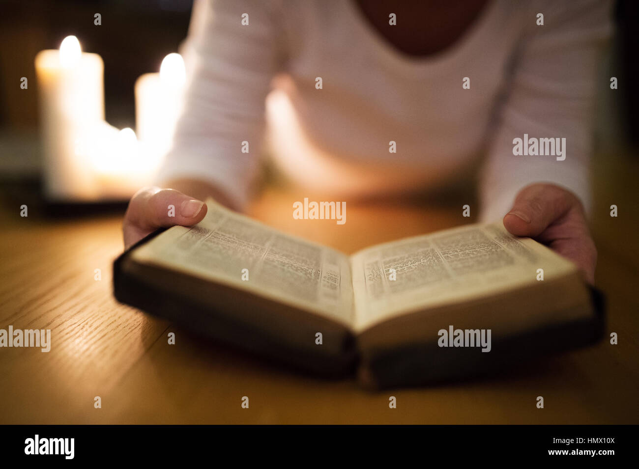 Nicht erkennbare Frau, die Bibel zu lesen. Brennende Kerzen neben ihr. Stockfoto