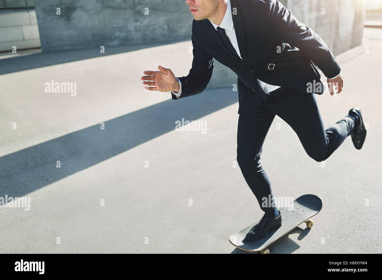 Vorderansicht eines Mannes im schwarzen Anzug gehen irgendwo auf einem skateboard Stockfoto