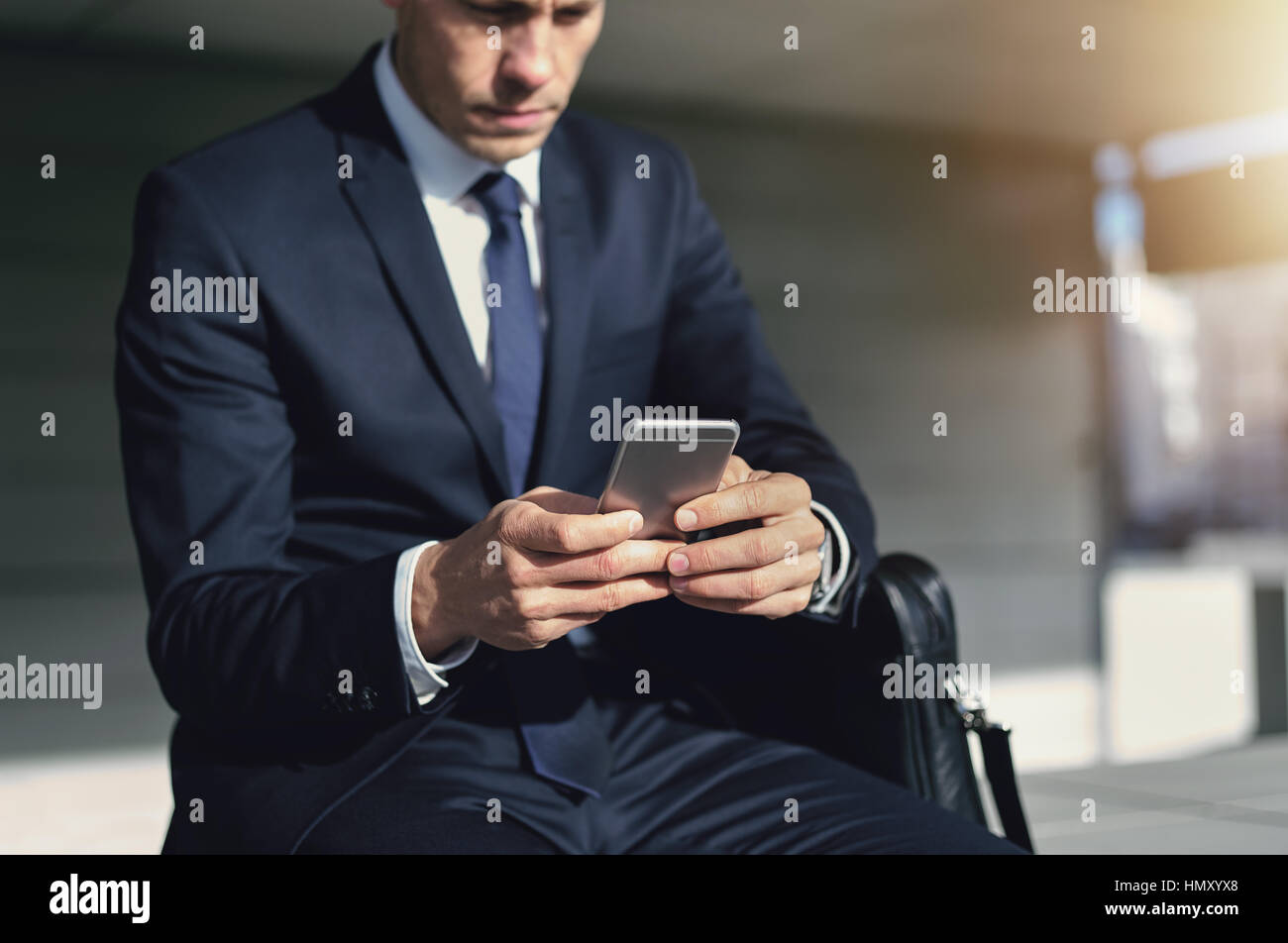 Junger Mann im dunklen Anzug, draußen zu sitzen und mit Smartphone mit Konzentration Stockfoto