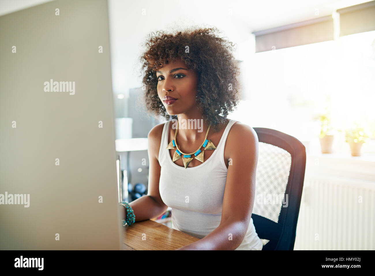 Ziemlich stylish junge afroamerikanische Frau arbeitet an einem großen Desktop-Monitor in einem hohen zentralen Büro lesen am Bildschirm Stockfoto