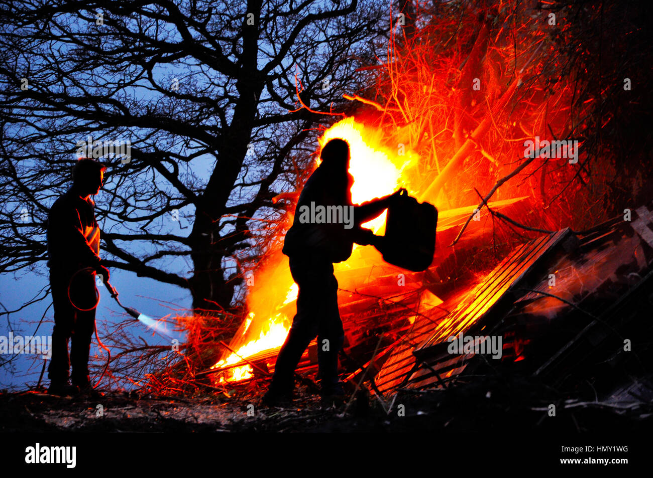 Silhouetten von Personen anzünden das Feuer vor einem großen Osterfeuer Stockfoto