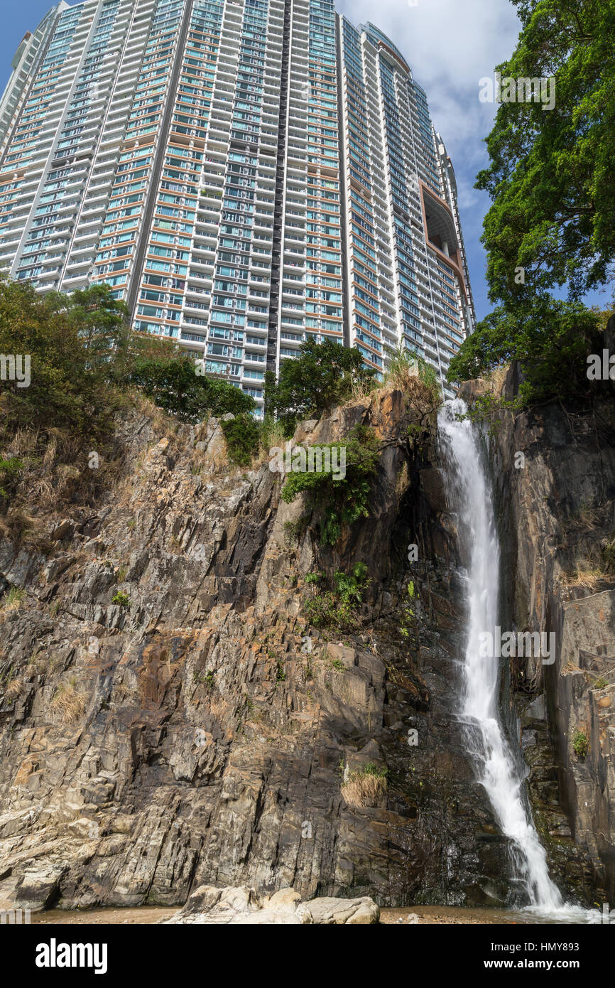Steilen Felsen, Wasserfall und einem Hochhaus Wohnung Ansicht von unten am Wasserfall Bay Park in Hong Kong, China. Stockfoto