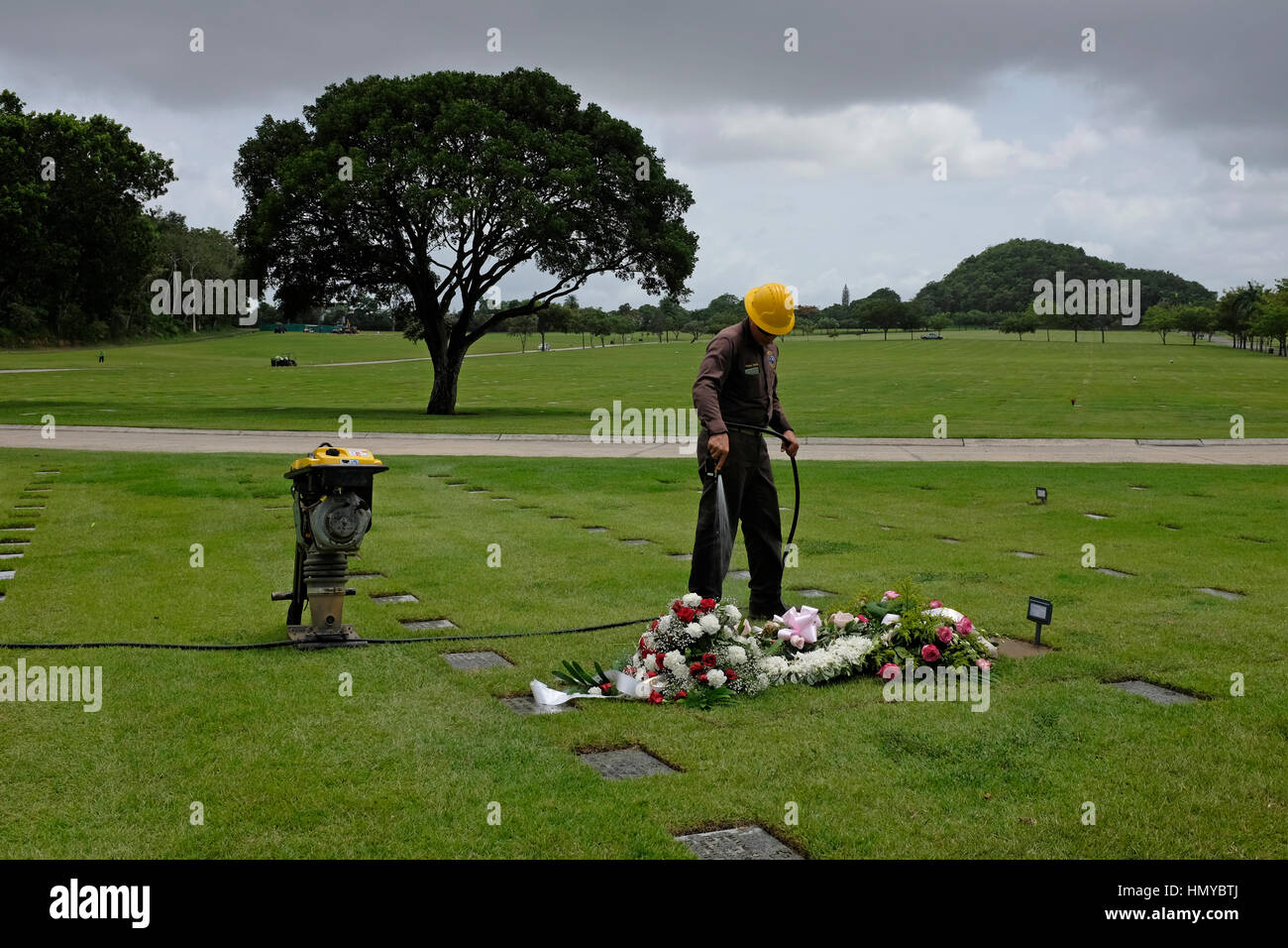 Ein Hausmeister Gewässer die Blüten an einem vor kurzem ausgegraben Grab auf dem Puerto Rico National Cemetery in Bayamon, Puerto Rico. Stockfoto