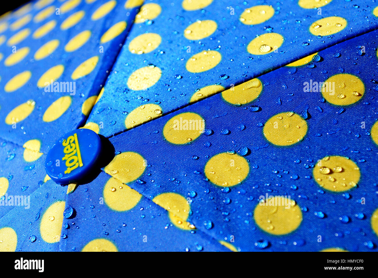 Regentropfen auf einen blauen und gelben Regenschirm. Stockfoto