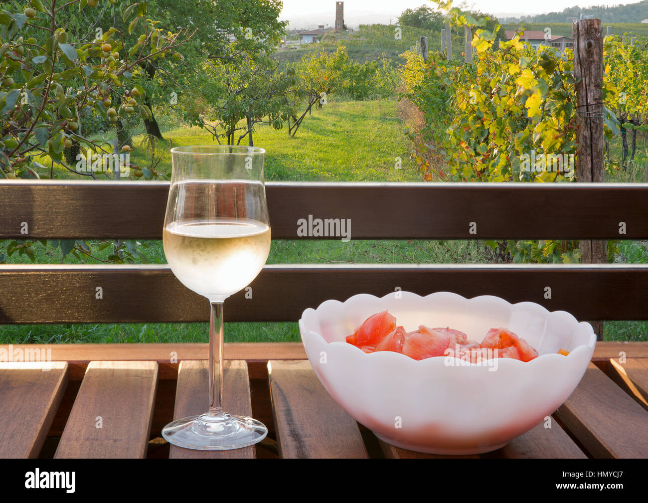 Glas Weißwein und frischen Tomaten Salat auf Holztisch mit malerischen mediterranen Ausblick im Hintergrund. Brda Region, westlichen Slowenien. Stockfoto