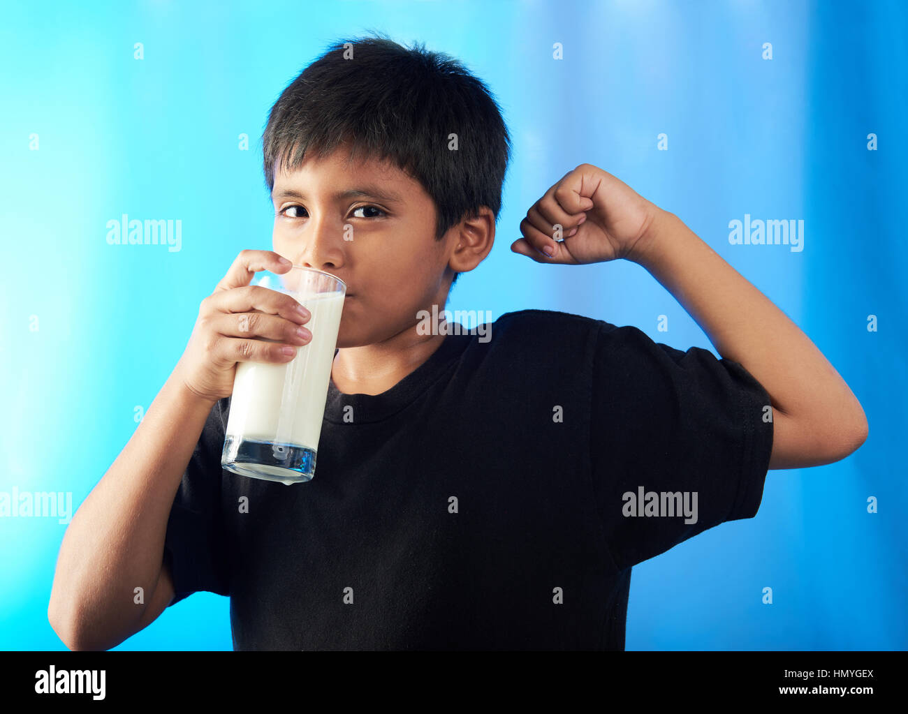 Latino Boy Milch trinken und zeigen Muskeln isoliert auf blau Stockfoto