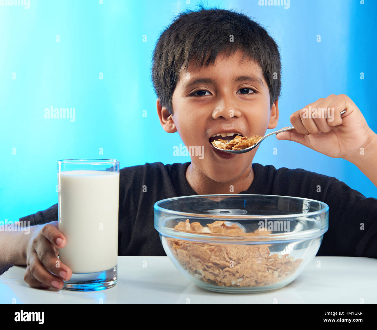 Latino Boy essen Müsli auf blauem Hintergrund isoliert Stockfoto