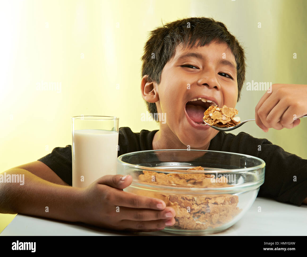 Junge mit Frühstück mit Müsli und Milch isoliert auf gelb Stockfoto