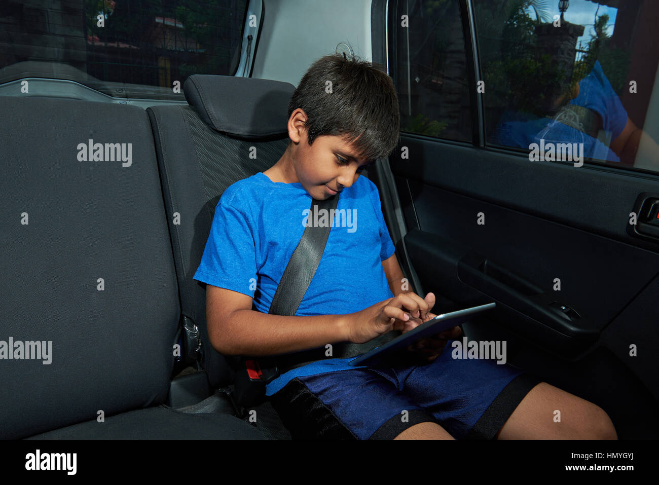 Latino Boy mit Tablette auf dem Rücksitz des Autos Stockfoto