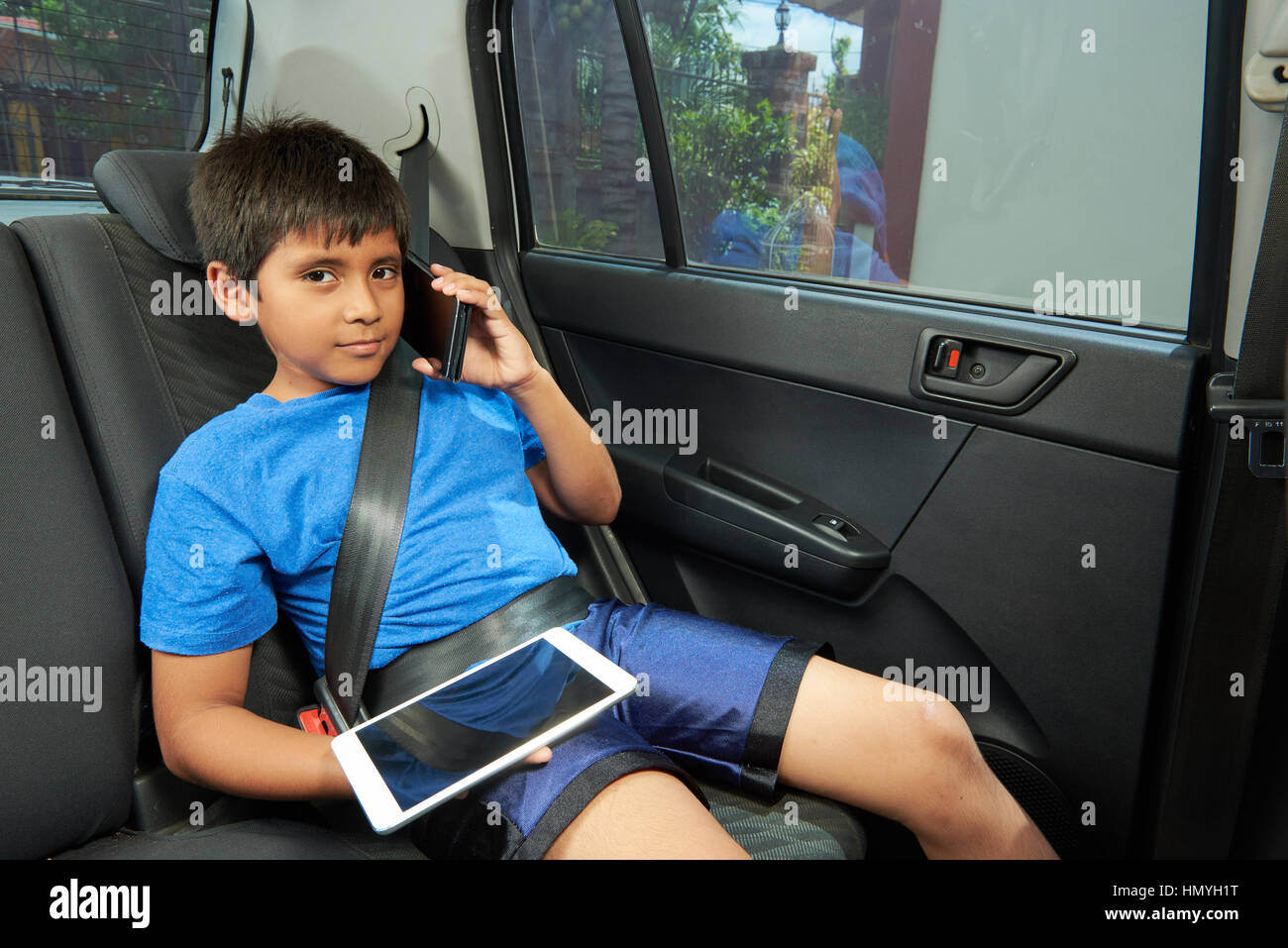Latino Boy mit Gadgets im Rücksitz des Wagens Stockfoto