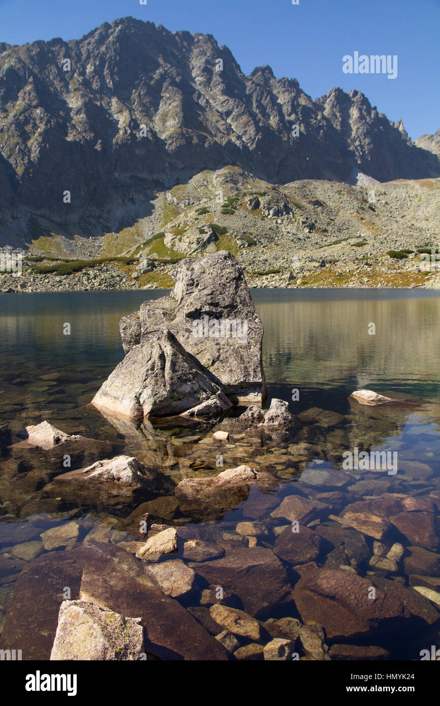 Felsen in einem ruhigen Bergsee vor dem Hintergrund einer zerklüfteten Bergkette zeigt die Schönheit unserer natürlichen Umwelt Stockfoto