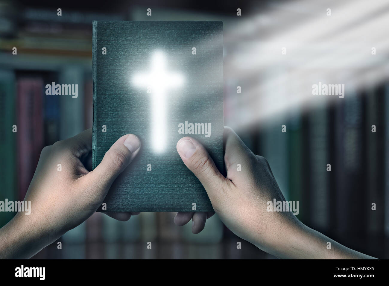 Magische Buch der Bibel mit magischen Kreuz Licht in der hand gegen die Regale mit Büchern, die Suche nach Informationen in einer Bibel, einem Leseraum in der Bibliothek und Stockfoto