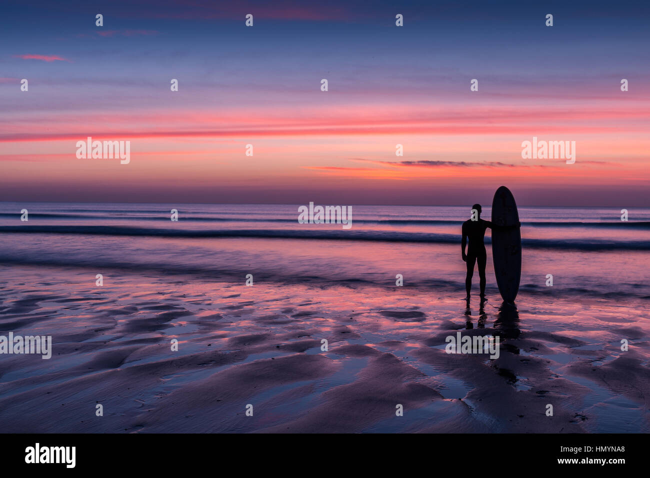 Surfer am Strand bei Sonnenuntergang stehend Stockfoto