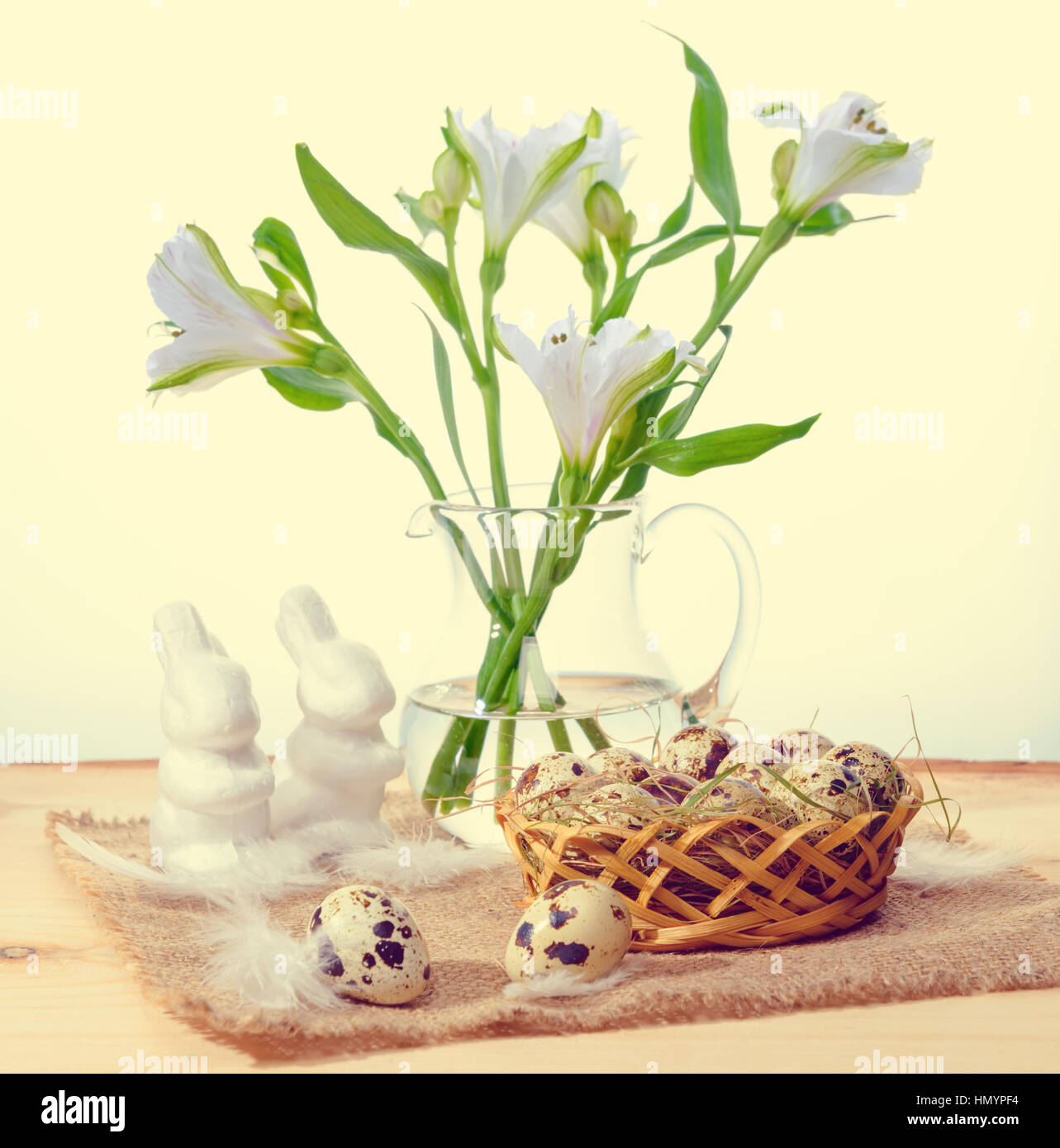 Wachteleier mit Stroh und Federn in Korb, Hasen weiß auf Sackleinen und Lilie Blumenstrauß in Vase, Ostern-Konzept Stockfoto