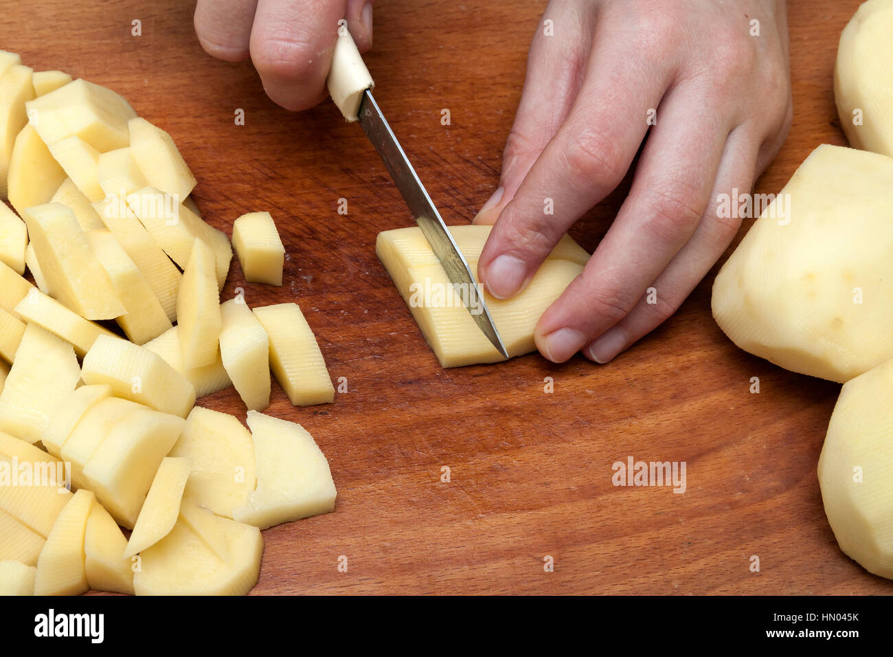 Zarte Frauenhand mit einem Messer schneiden schneiden Kartoffeln auf Holzbrett in Küche. Gesunde Ernährung und Lebensweise. Ansicht von oben Nahaufnahme Stockfoto