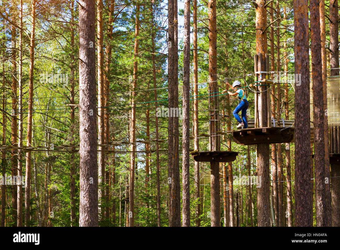 Teenager-Mädchen geht auf aufklappbaren Spuren in extremen Seil Park im Sommer Wald. Höhentraining Klettern Kindes dran Adventure – ausgestattet mit sa Stockfoto