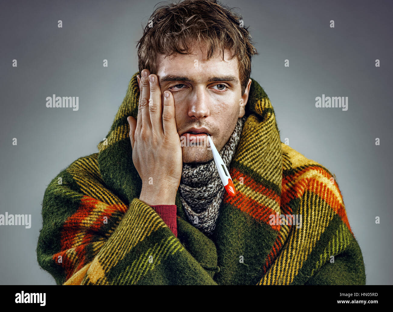 Kranker junge Mann mit einem Thermometer im Mund gewickelt in Karo. Medizinisches Konzept Stockfoto