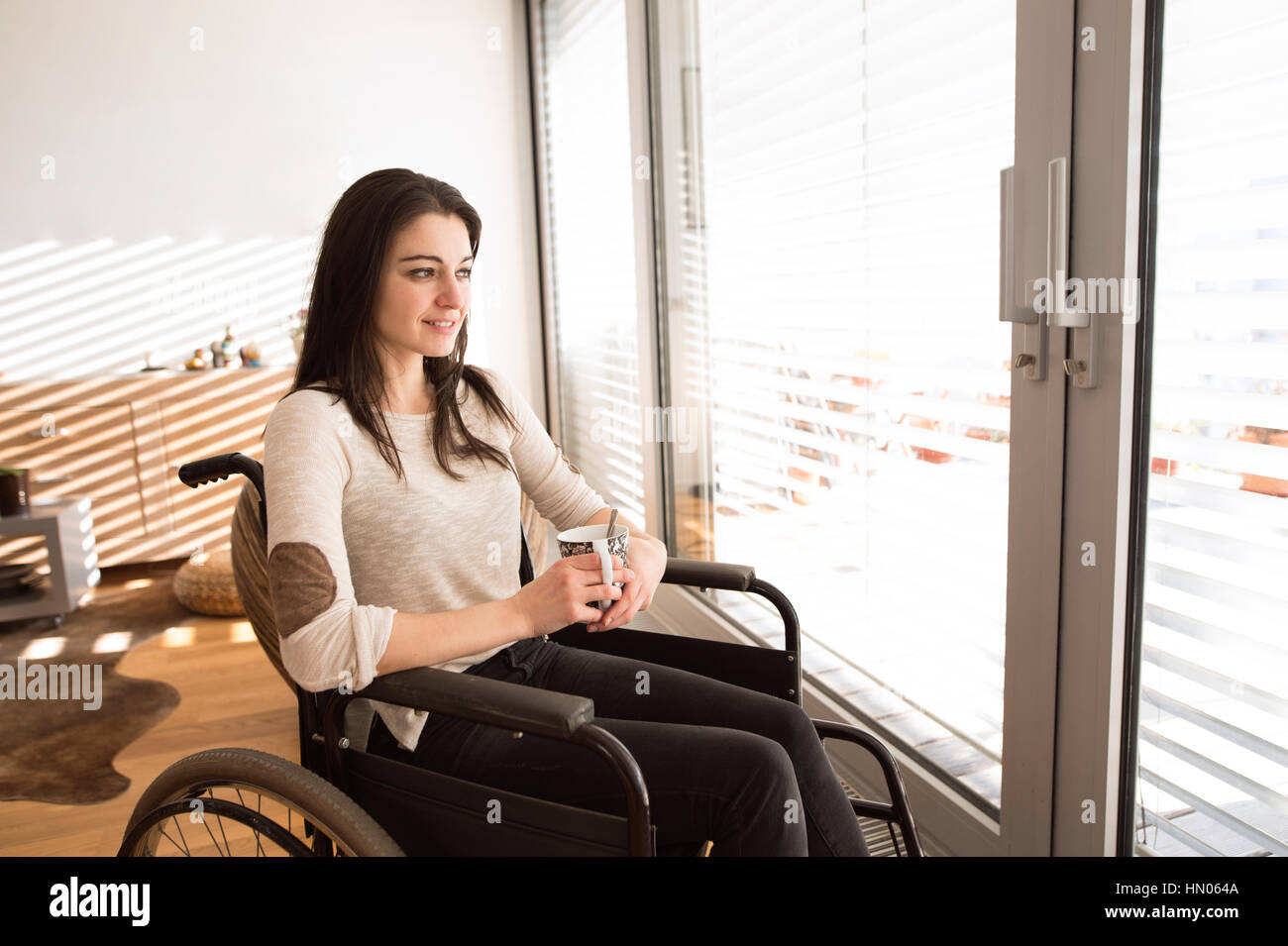 Schöne junge behinderte Frau im Rollstuhl zu Hause. Stockfoto
