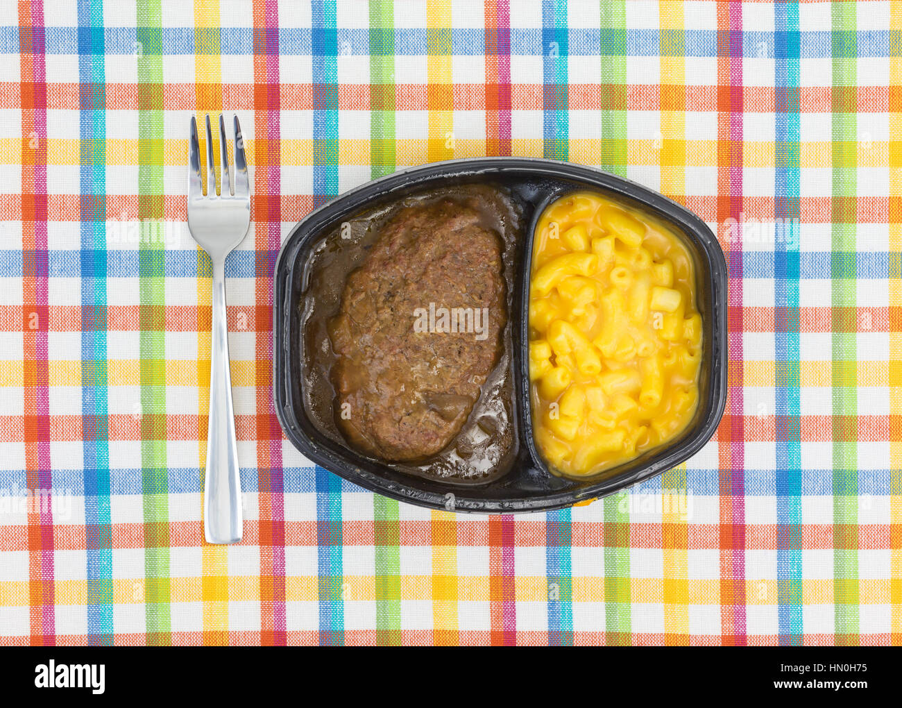 Draufsicht auf ein TV-Diner Essen von Salisbury Steak mit Gravy Makkaroni und Käse in einer schwarzen Schale mit einer Gabel auf die Seite auf einem bunten Tischset. Stockfoto