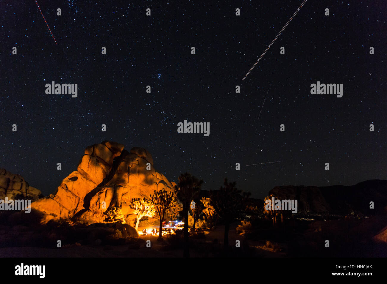 Ein Lagerfeuer beleuchtet die Felsen im Hidden Valley Campground im Joshua Tree National Park mit mehreren Sternen Gemeinkosten. Stockfoto