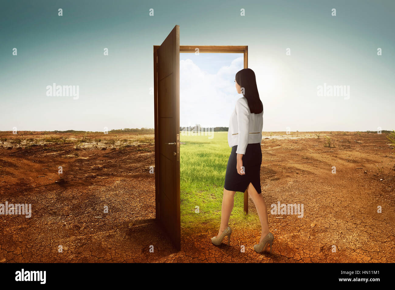 Junge asiatische Geschäftsfrau zu Fuß auf die offene Tür nach grünen Umgebung am gebrochenen Land Hintergrund Stockfoto