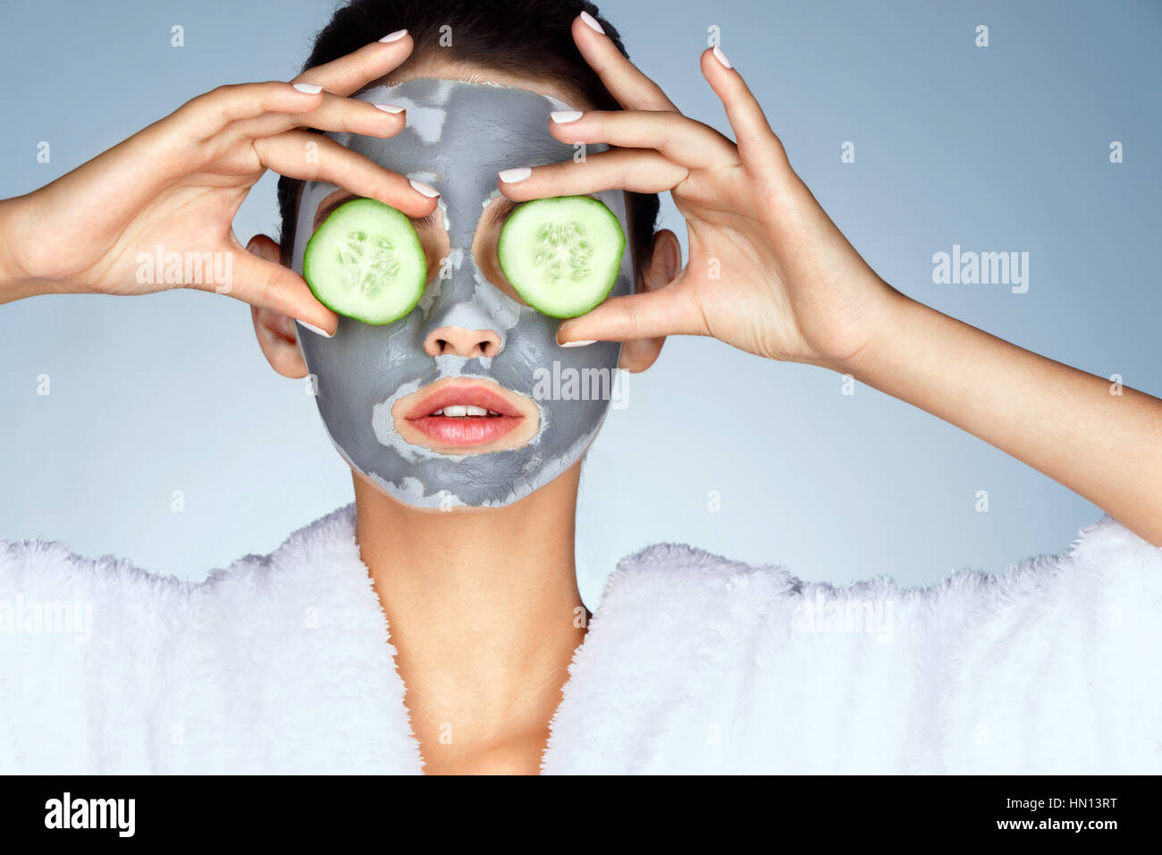 Junge Frau mit einer Gesichtsmaske. Foto von attraktiven jungen Frau, die für ihre Augen mit Gurken auf blauem Grund. Pflege selbst Stockfoto