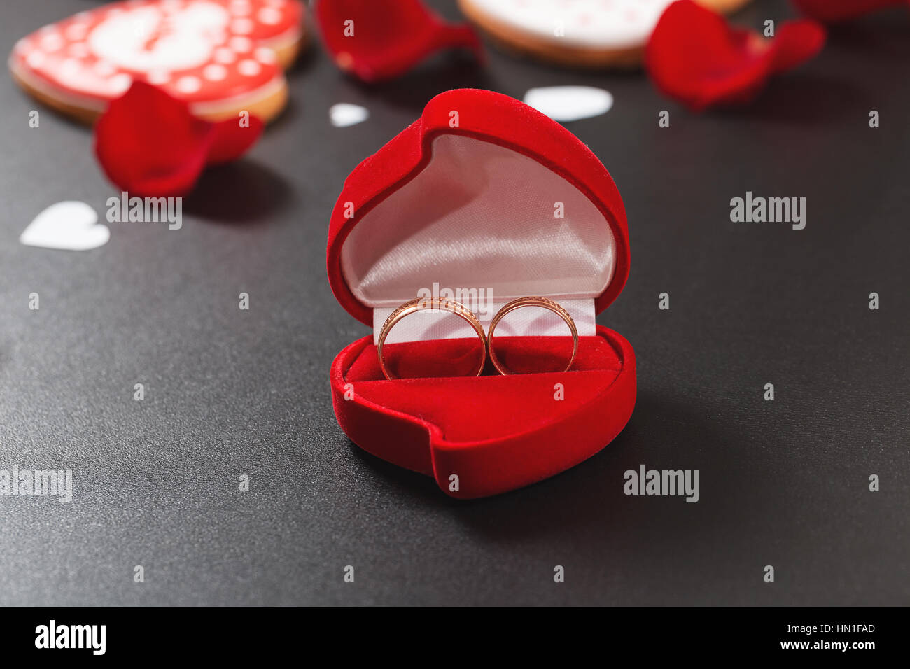 Schöne rote Rosen Blütenblätter und Trauringe auf einem schwarzen Hintergrund. Postkarte zum Valentinstag oder Hochzeit. Freiraum für text Stockfoto