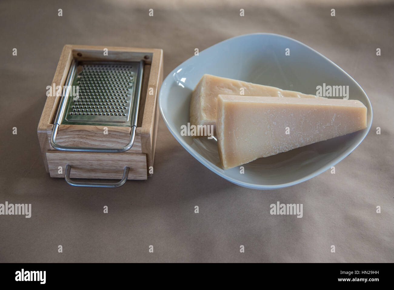 Stücke von Parmesan auf einem Teller neben einer hölzernen Käsereibe Stockfoto