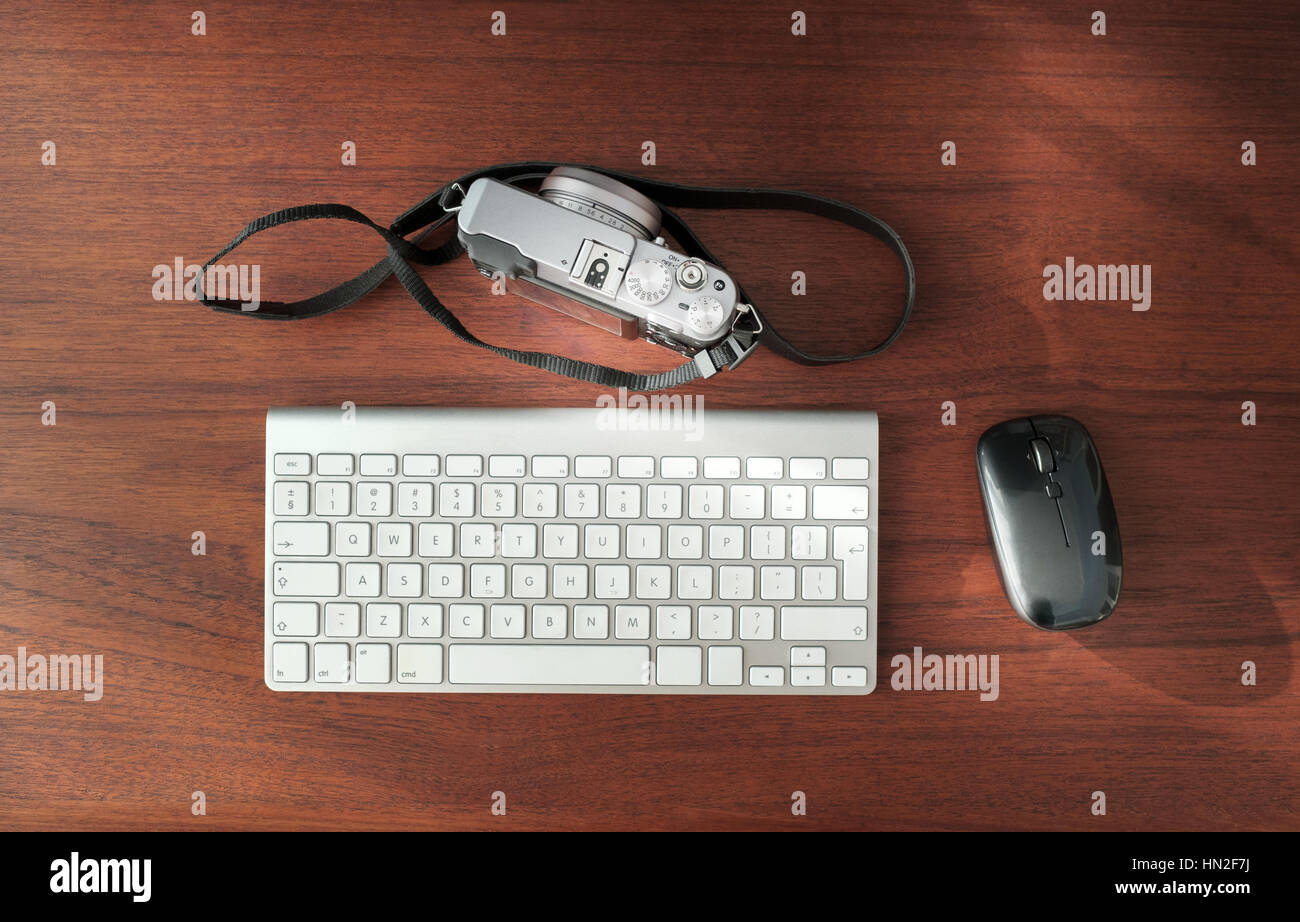 Spiegellose Digitalkamera, drahtlose Maus und Tastatur auf braunen Holz Schreibtisch Stockfoto