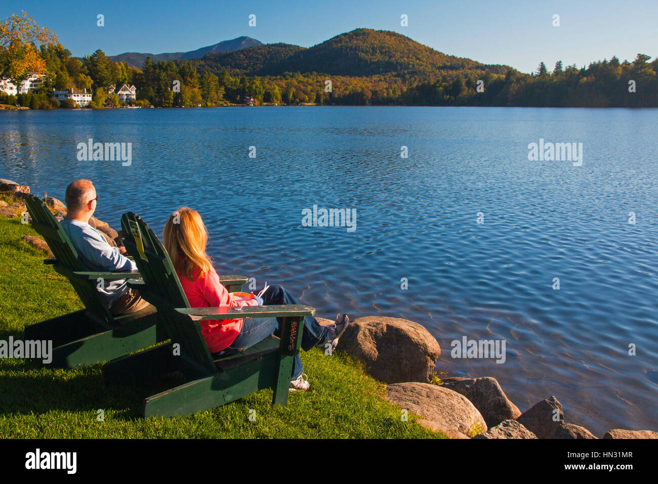 Paar in hölzerne Adirondack Stühle wacht über Mirror Lake in den Adirondack Mountains in Lake Placid, nördlichen New York in den Vereinigten Staaten Stockfoto