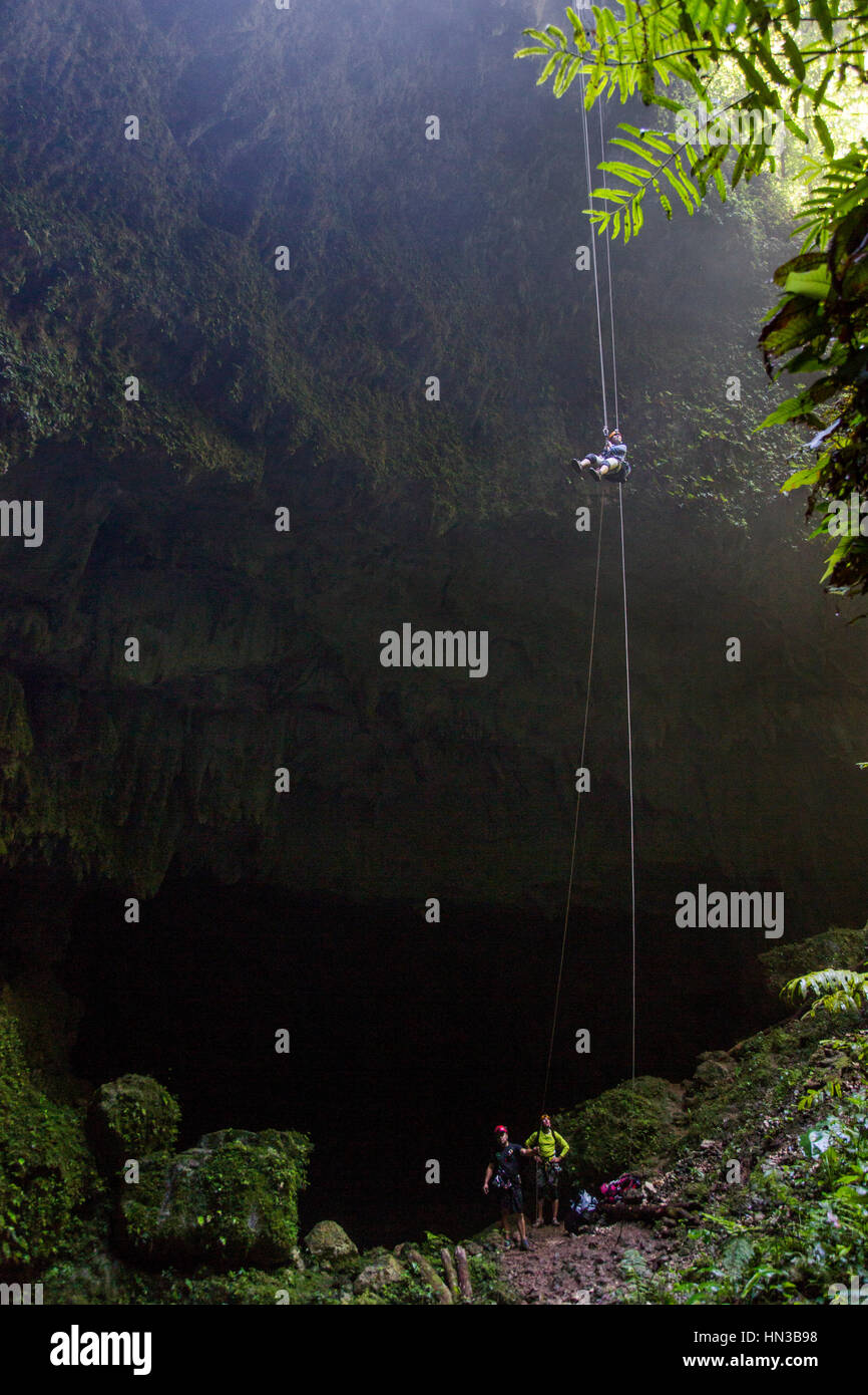 Eine junge Frau Abseilen in eine tiefe dunkle Höhle In einem Wald In Puerto Rico Stockfoto