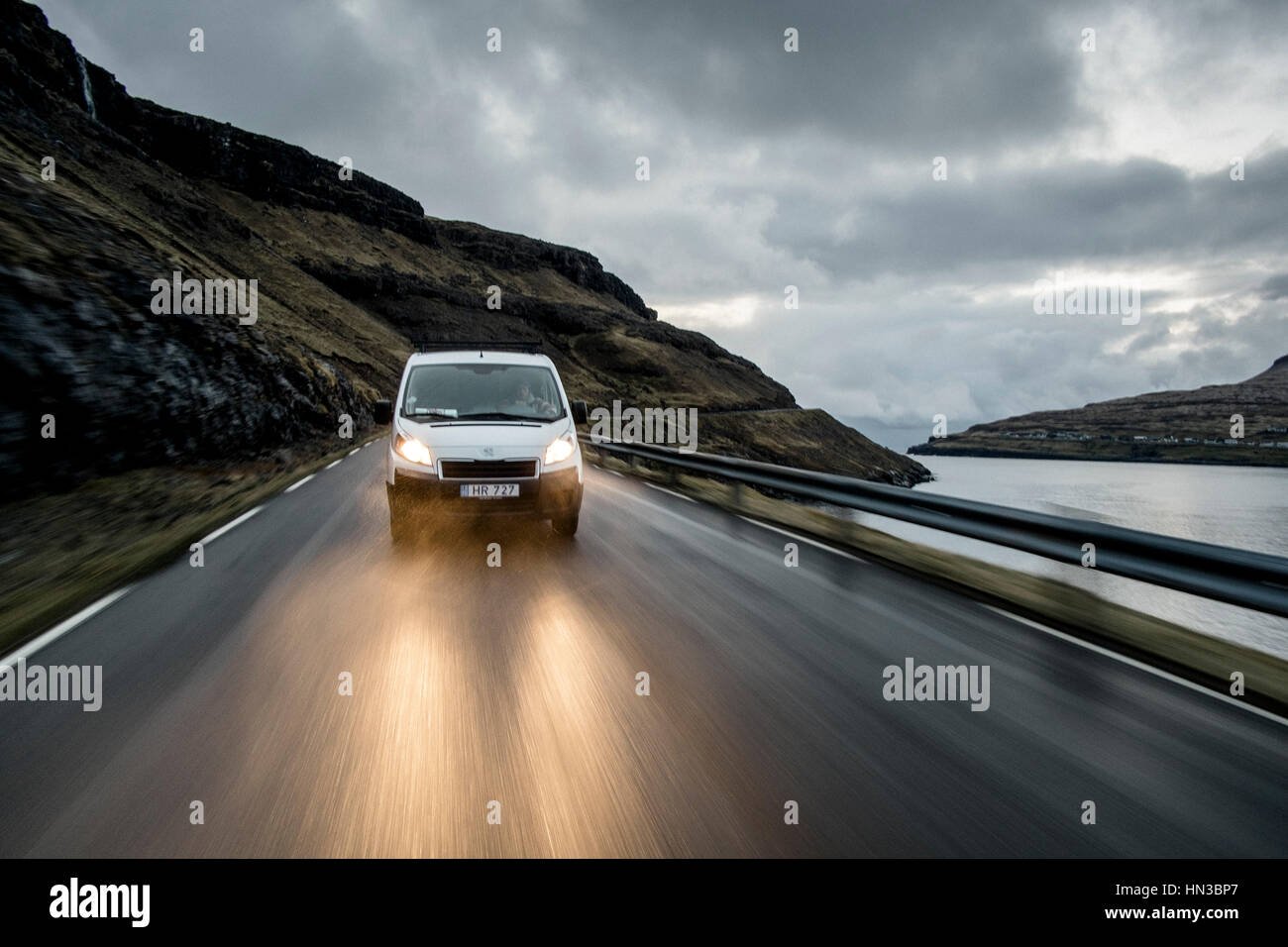 Ein weißes Auto fährt schnell auf einer nassen Straße vor Einbruch der Dunkelheit Stockfoto