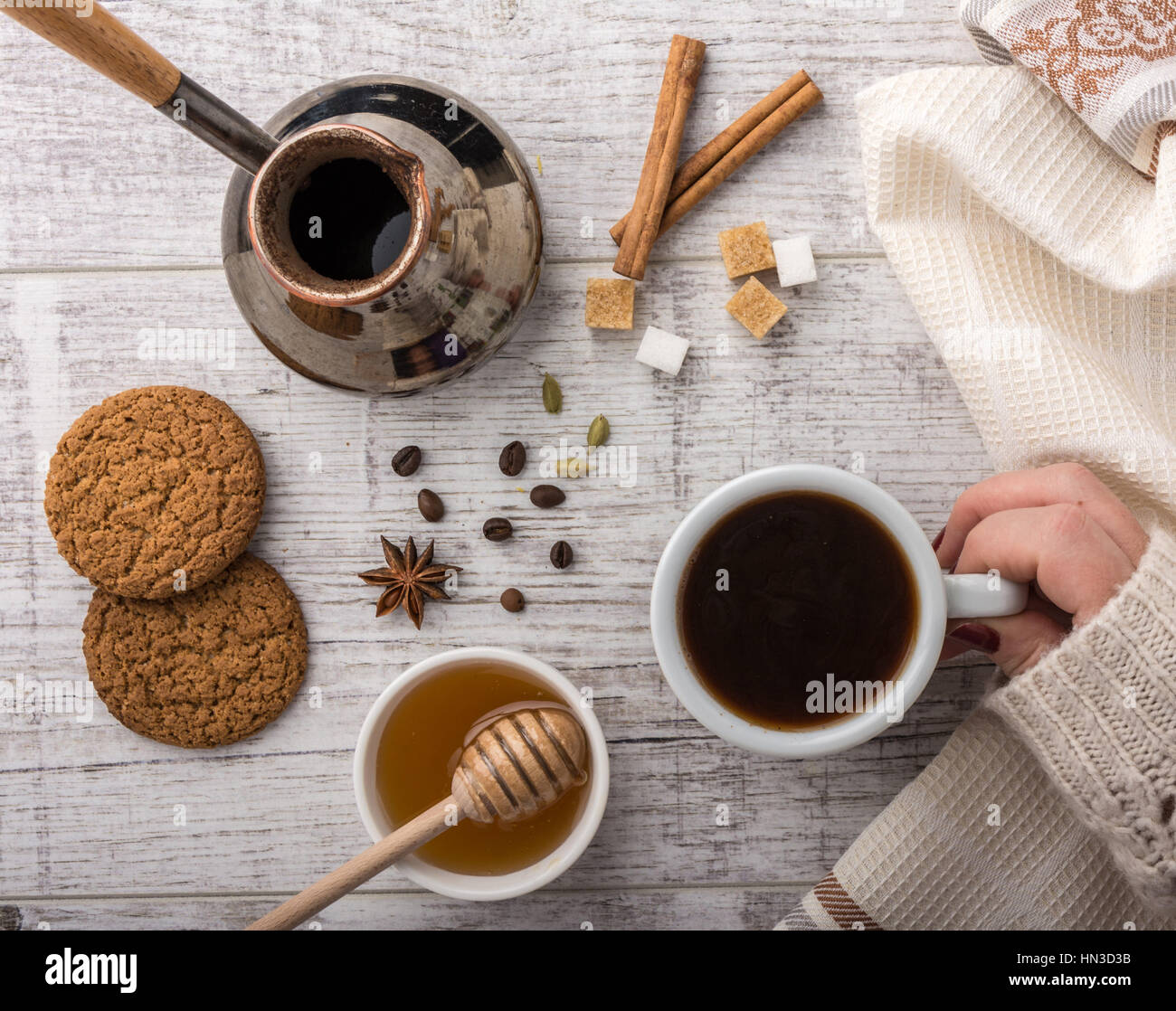 Frau trinkt Kaffee mit Keksen, Zucker und Honig. Kaffeemaschine, Zimt, Sternanis und Kardamom auf einem weißen Holztisch liegen. Stockfoto