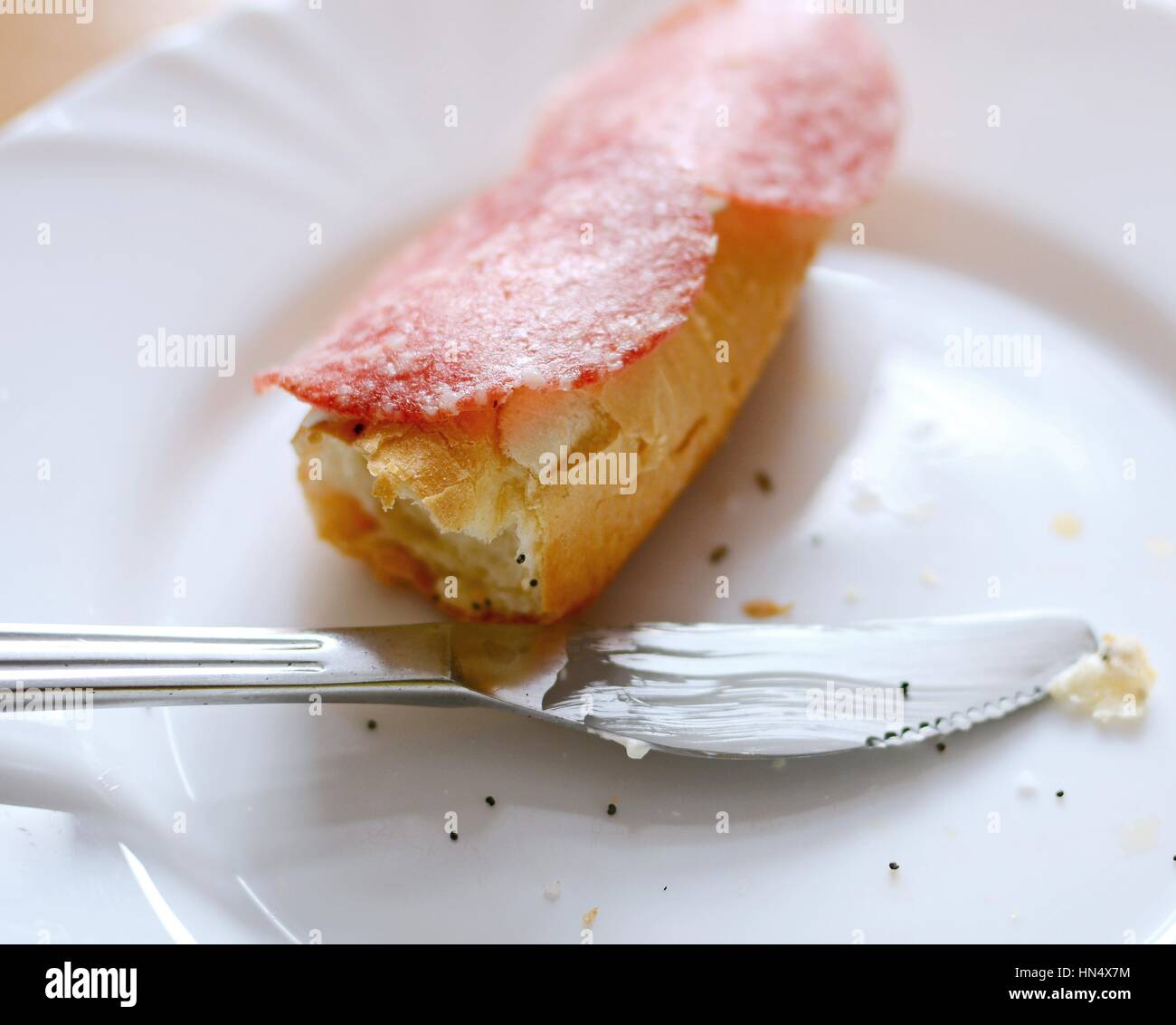 Überbleibsel der Salami Brot Brötchen mit Biss fehlt und Messer auf einem weißen Teller liegen. Stockfoto