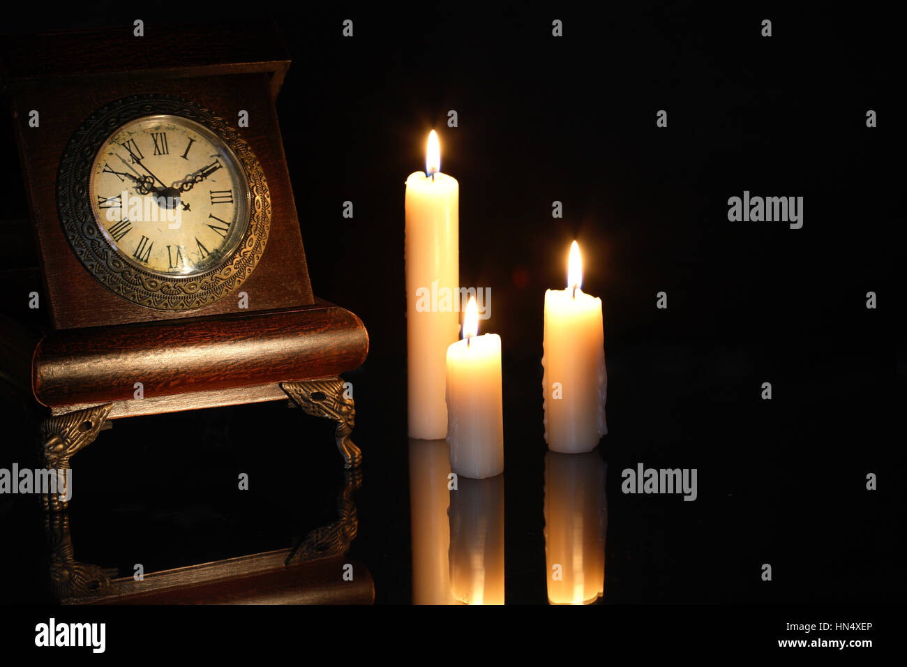 Vintage Holz Uhr in der Nähe von Anzünden von Kerzen auf dunklem Hintergrund Stockfoto