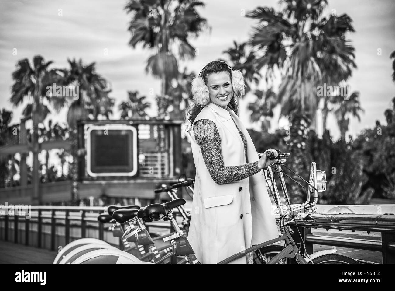 in Barcelona für einen perfekten Winter. Porträt von glücklich modern Fashion Monger in Ohrenschützer in Barcelona, Spanien stehen in der Nähe von Fahrrad Stockfoto