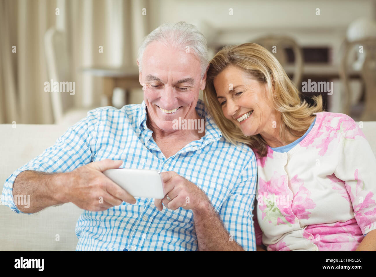 Älteres paar Überprüfung lächelnd eingefangen Fotos auf Handy im Wohnzimmer zu Hause Stockfoto