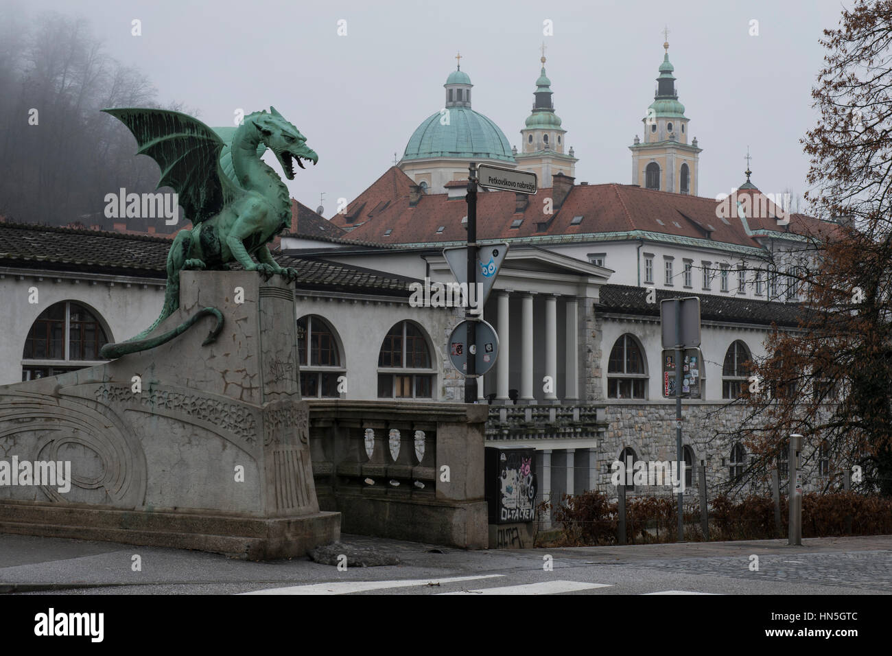 Eines der Drachen-Skulpturen von der Drachenbrücke vor der Zentralmarkt und die St.-Nikolaus-Kathedrale. Altstadt, Ljubljana, Slowenien. Stockfoto