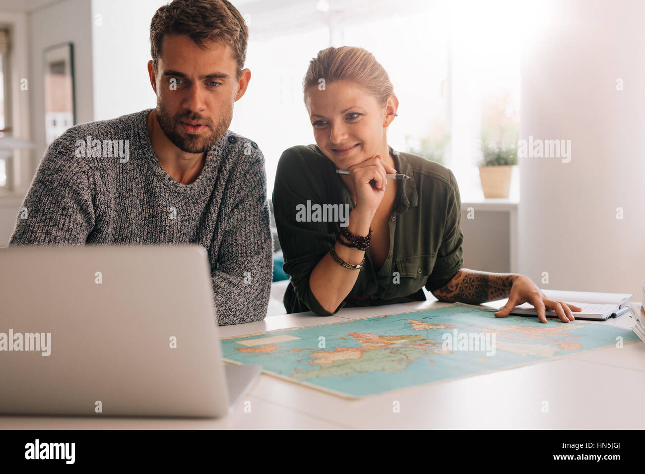 Junger Mann und Frau betrachten Laptop-Computer mit Weltkarte vor. Paar mit Technologie, um die Welt zu erkunden. Stockfoto