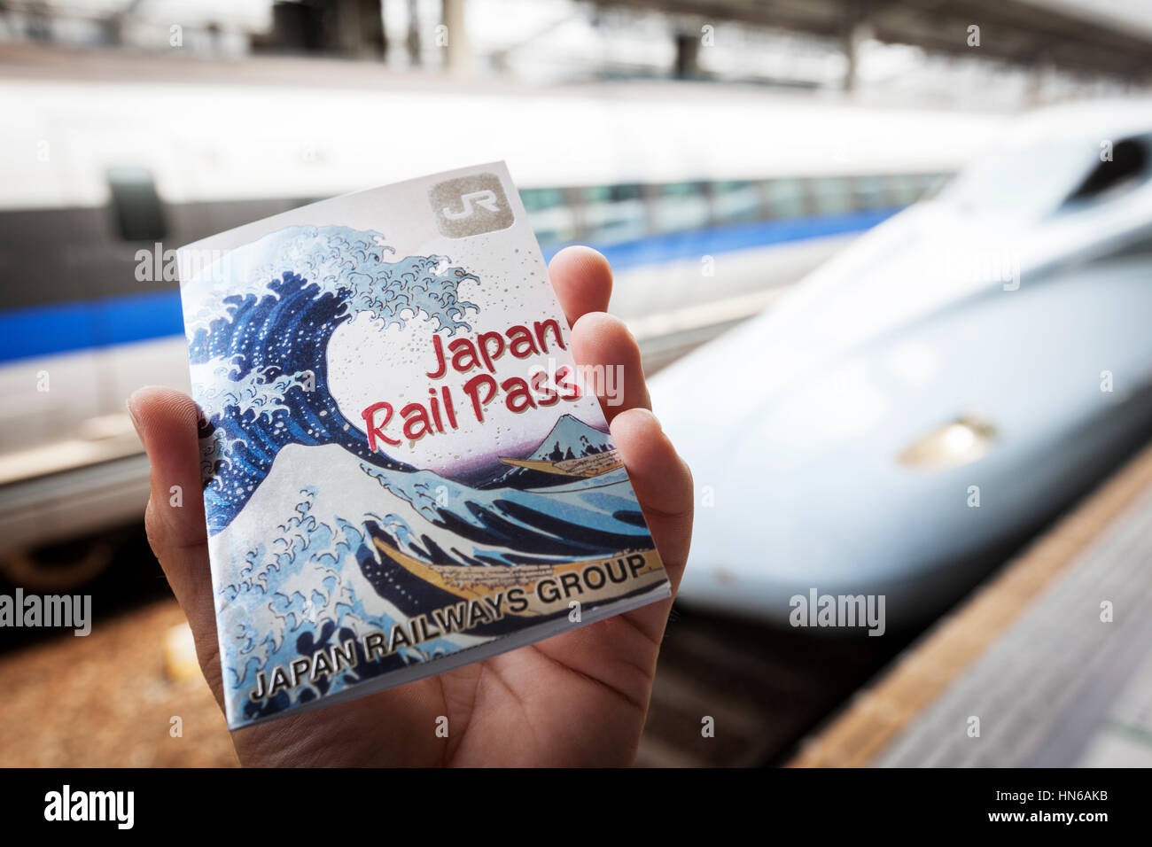 Okayama, Japan - 8. Mai 2012: Nahaufnahme einer männlichen Hand hält einen Japan Rail Pass am Bahnhof Okayama mit Shinkansen-Züge im Hintergrund. Die Stockfoto