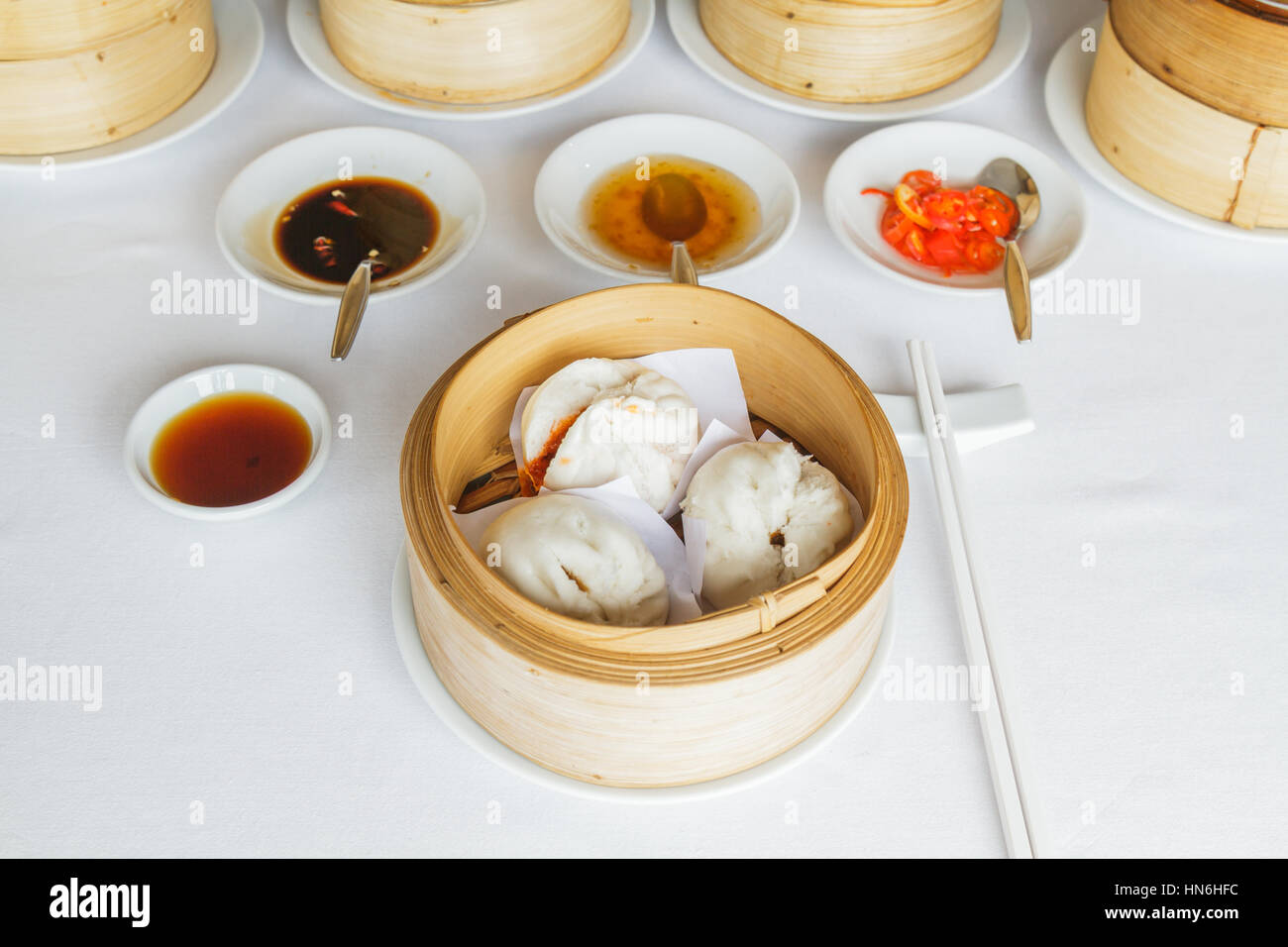 Dim Sum Essen dampfgegarte Grill Schweinefleisch Brötchen im Bambuskorb im Restaurant mit Sojasauce, süße Sauce, Chili-Sauce und Stäbchen. Stockfoto