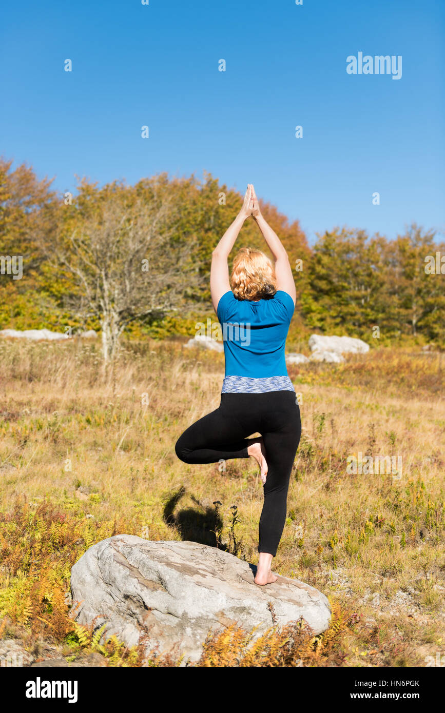 Junge Frau in Baum-Yoga-Pose stehen auf einem Bein auf Felsen Stockfoto