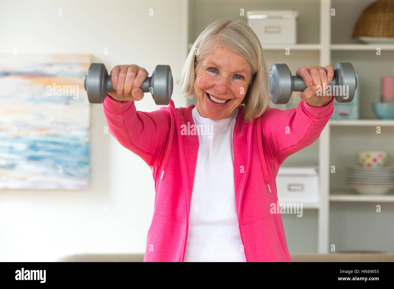 Ältere Dame lächelnd in die Kamera, während Sie Hanteln benutzen. Stockfoto