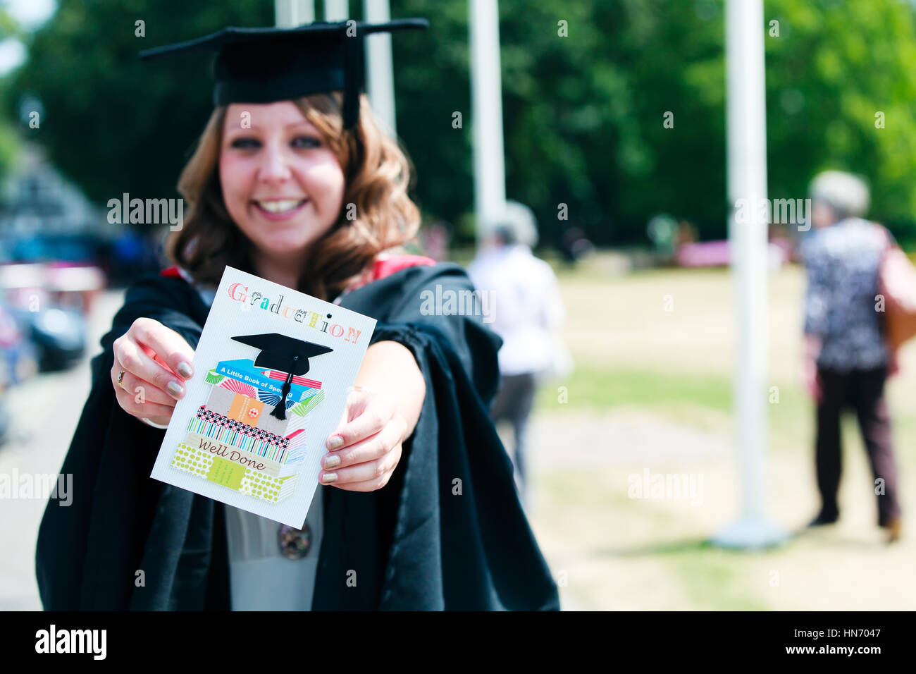 Eine Universitätsabgängerin, die ein Mörtelbrett und ein Kleid trägt, hält eine gut ausgemachte Karte an ihrem Abschlusstag Stockfoto