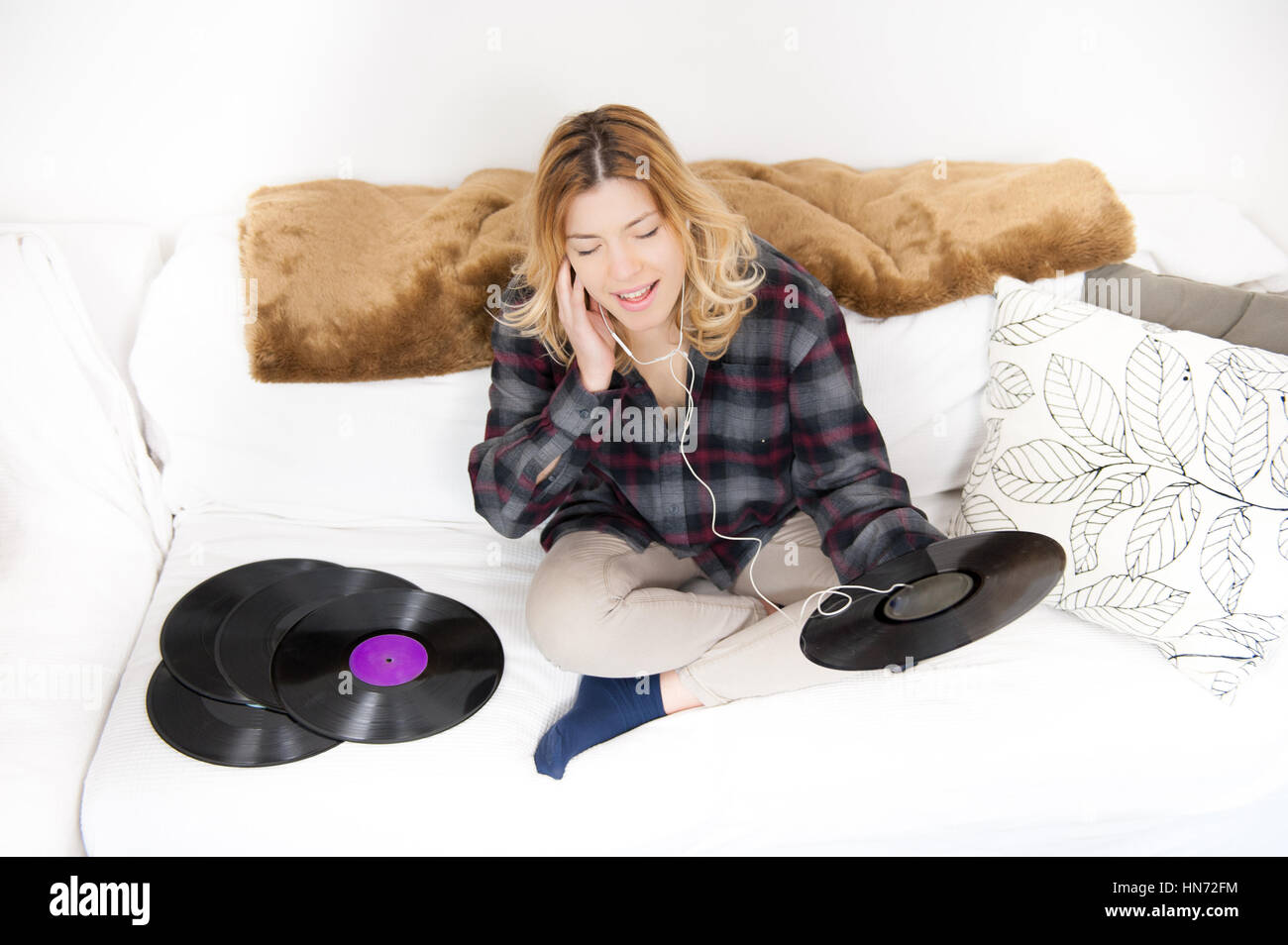 Junge blonde Frau glücklich genießen Musik hören von Vintage Vinyl-Schallplatten auf Sofa im Wohnzimmer Stockfoto