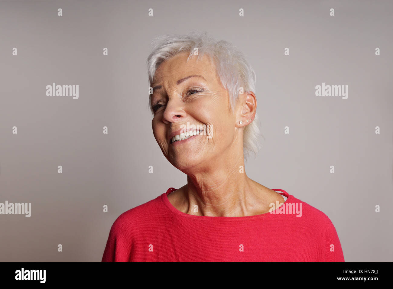 glückliche ältere Frau mit trendigen kurze weiße Haare zu lachen. Grauer Hintergrund mit Textfreiraum. Stockfoto